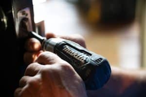 Close-up of a contractor’s hands as they use a power drill to repair a doorknob