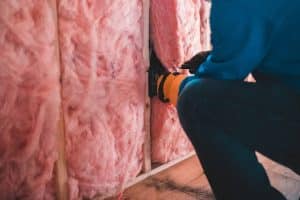 Close-up of a contractor installing pink fiberglass wall insulation